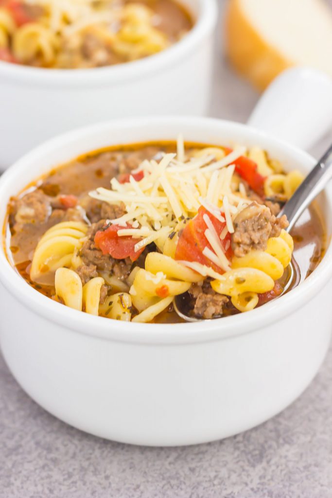 a spoon digging into a white bowl of lasagna soup