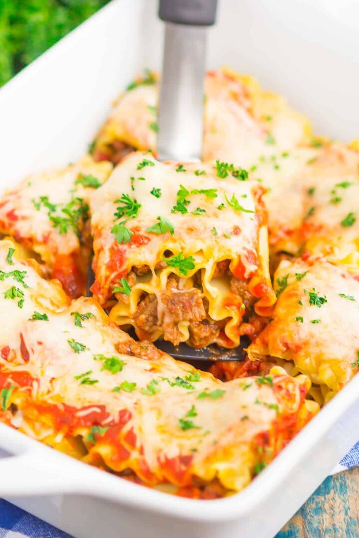 lasagna rolls in a white dish with a spatula holding up one piece