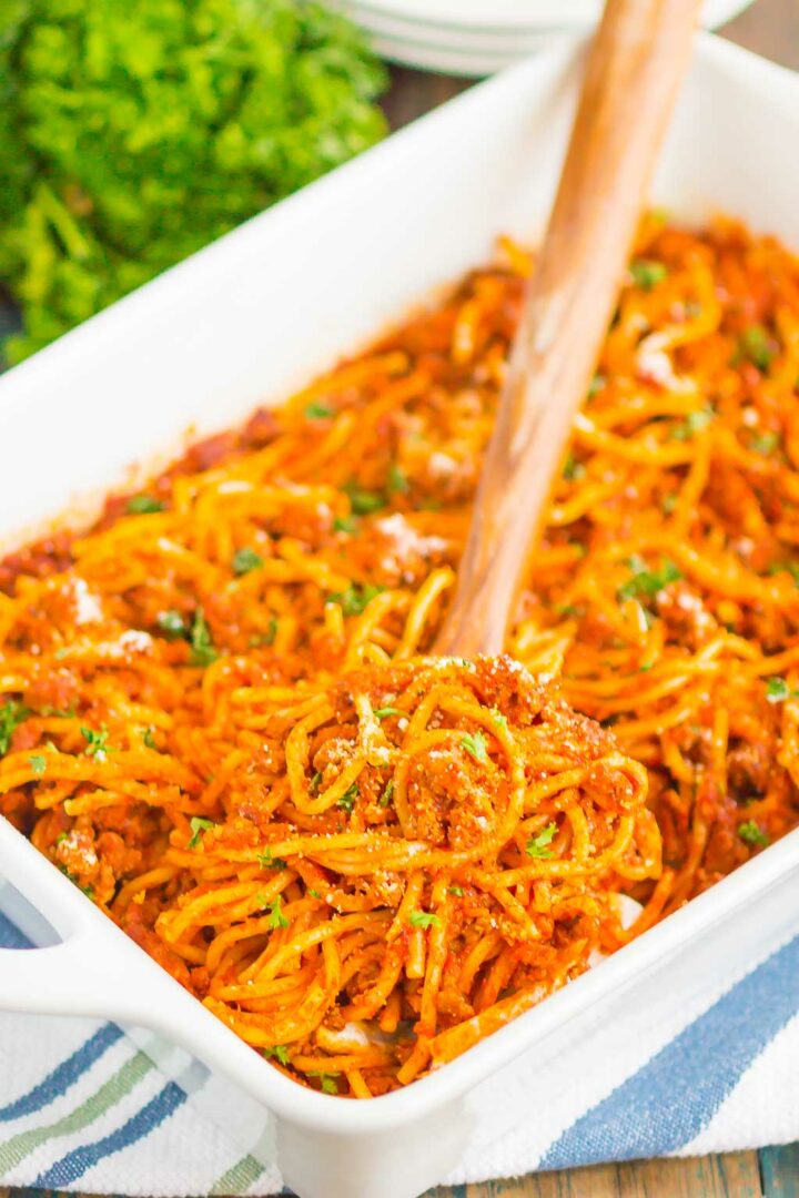 spaghetti in a white dish with a wooden spoon showing a big spoonful