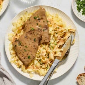 round steak with gravy on top of noodles on a white plate