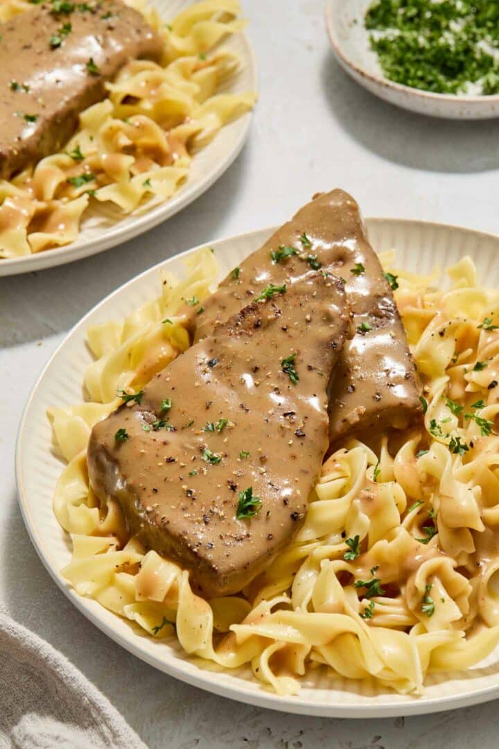 round steak with gravy on top of noodles on a white plate