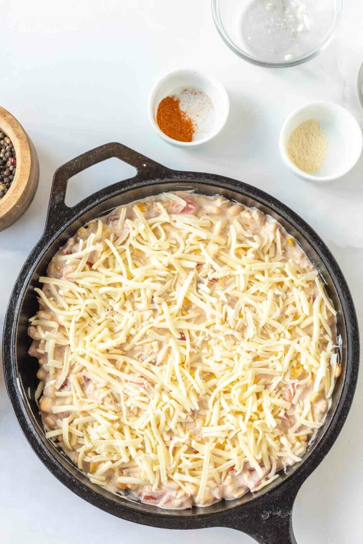 corn dip in a black skillet with shredded cheese on top