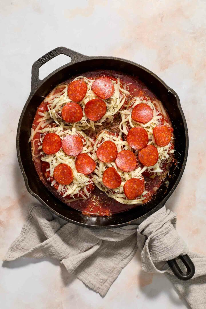 chicken in a black skillet with pepperoni and sauce