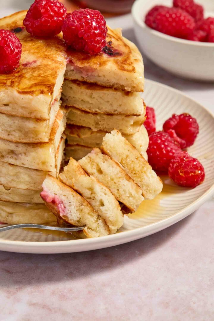 a forkful of pancakes shown on a white plate with a stack of pancakes