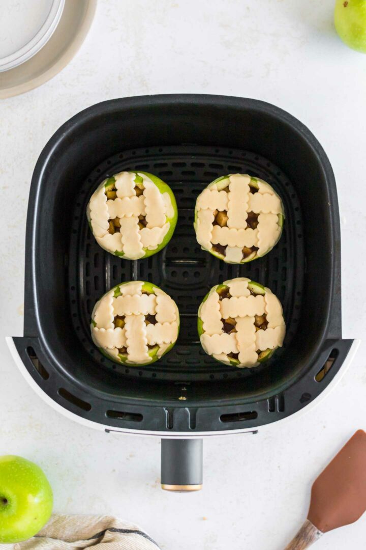 four apples with a lattice pie crust on top in the air fryer basket