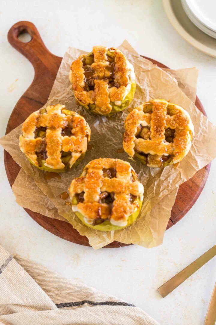 four baked apples with lattice pie crust on top on a wooden board