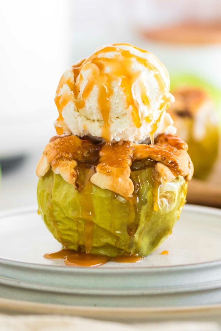 baked apple on a white plate with a scoop of vanilla ice cream and caramel drizzle