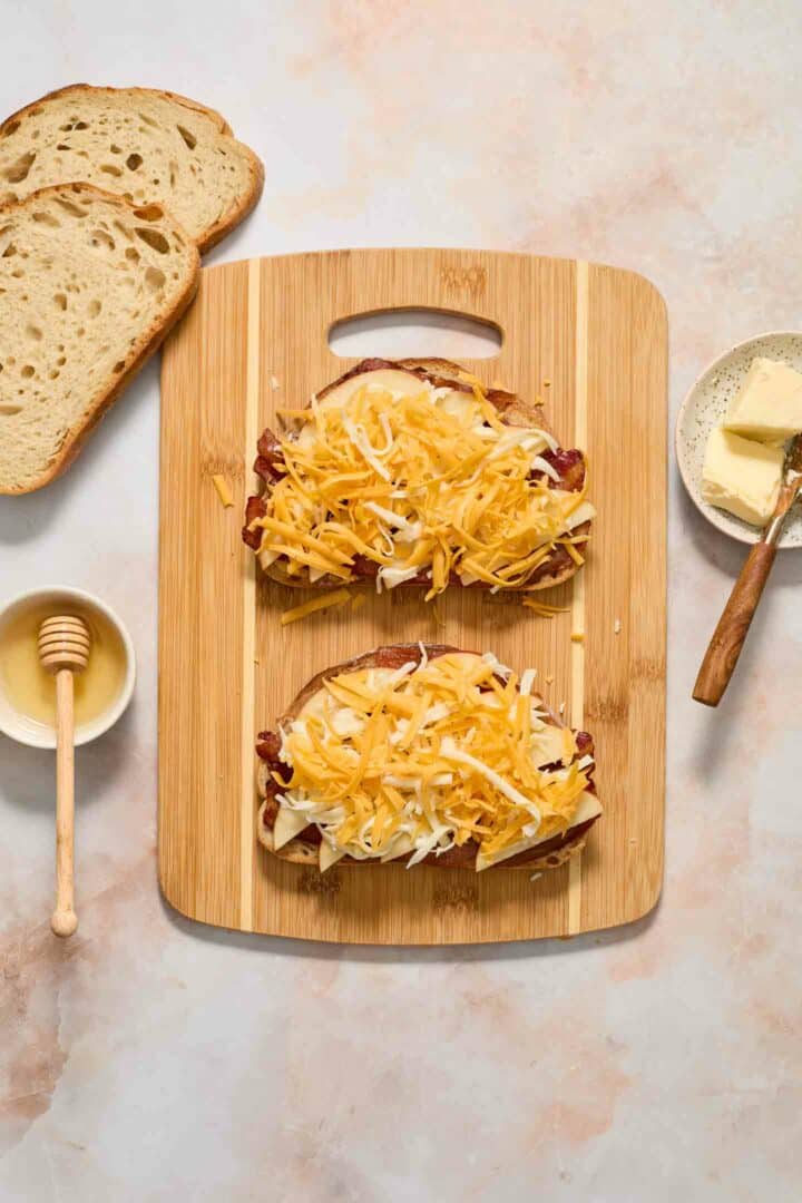 bread slices with bacon, honey, apples and cheese on a cutting board