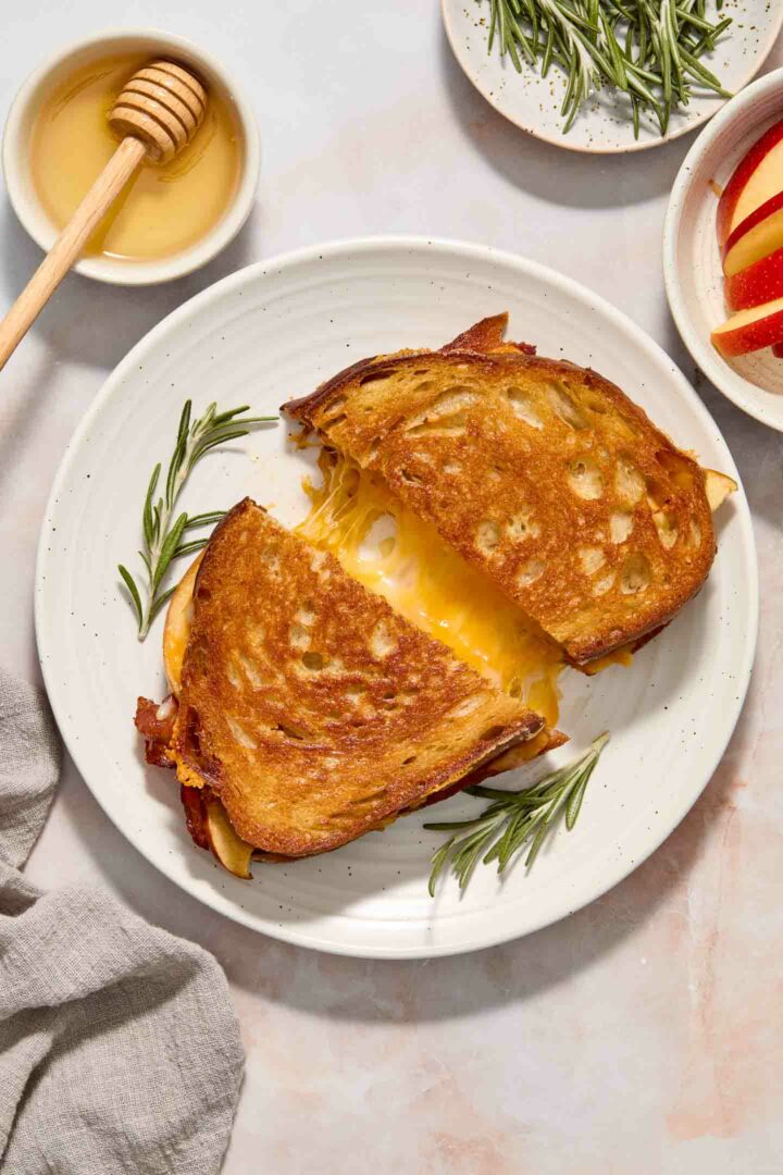 grilled cheese cut in half on a white plate with cheese oozing out