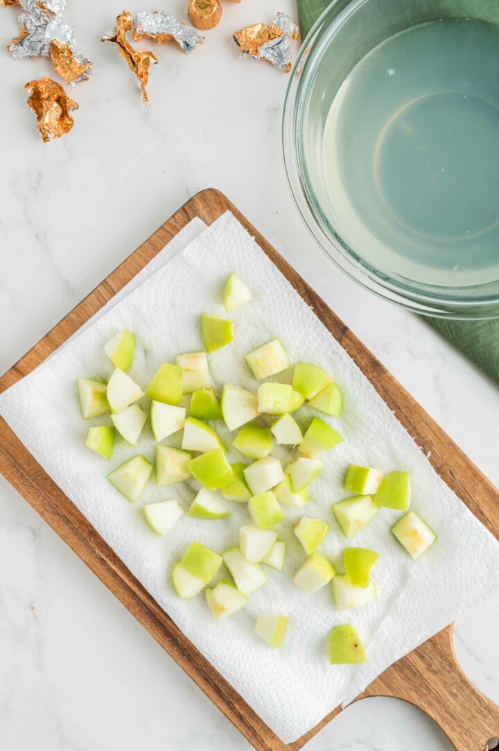 apple slices cut into cubes on a brown cutting board with parchment paper