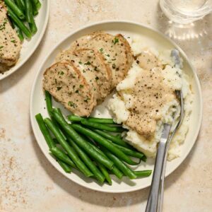 pork tenderloin with cream sauce on a white plate with mashed potatoes and green beans