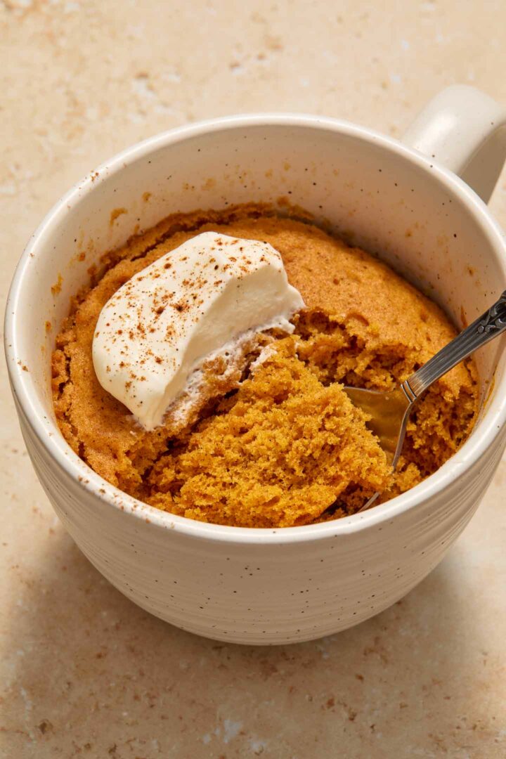 cake in a white mug with whipped cream and a spoonful of cake