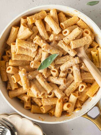 pumpkin alfredo pasta in a white skillet with a sprig of sage