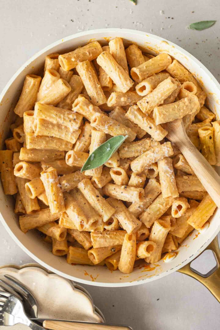 pumpkin alfredo pasta in a white skillet with a sprig of sage