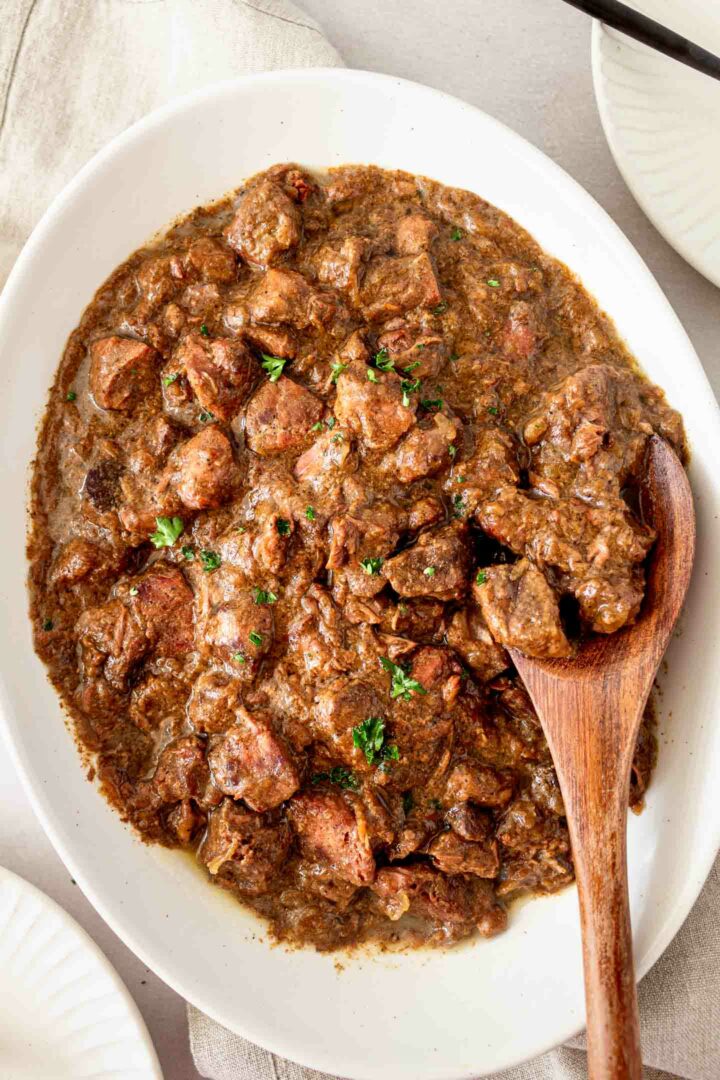 steak bites in a white serving dish showing a few pieces of steak bites on a wooden spoon