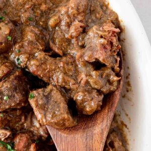 steak bites in a white dish with a wooden spoon shown with a few steak bites