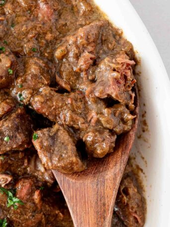 steak bites in a white dish with a wooden spoon shown with a few steak bites