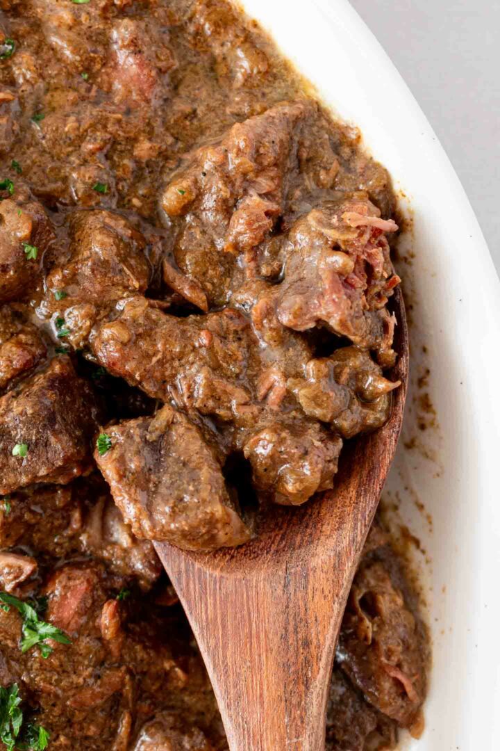 steak bites in a white dish with a wooden spoon shown with a few steak bites