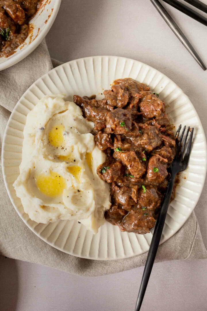 steak bites and mashed potatoes with butter on a white plate with a black fork