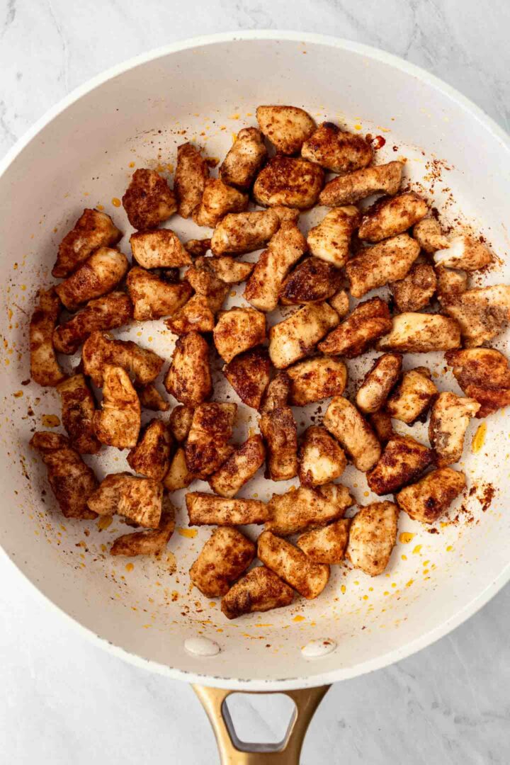 chicken cut into bite-sized pieces being cooked in a white skillet