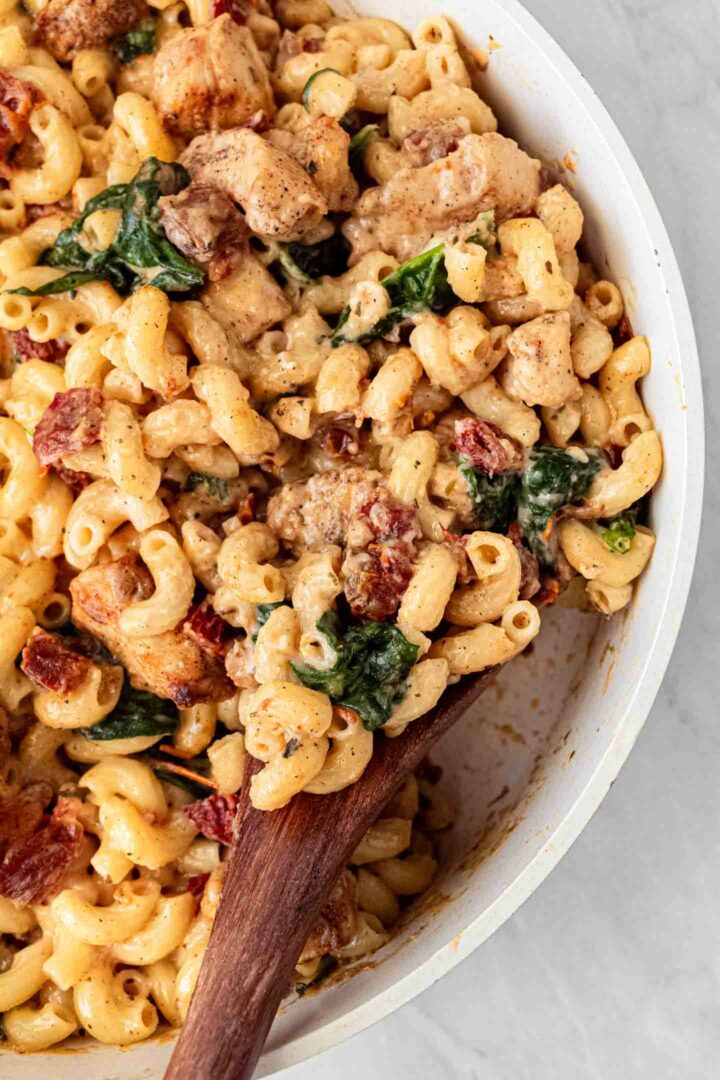 chicken mac and cheese in a white serving bowl with a wooden spoon