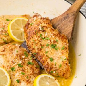 chicken in a white pan with a wooden spoon lifting a piece of chicken