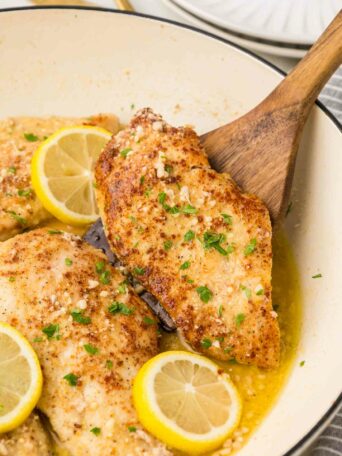 chicken in a white pan with a wooden spoon lifting a piece of chicken