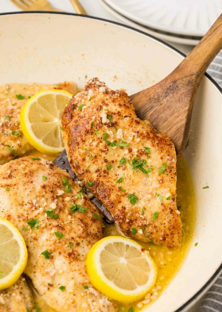 chicken in a white pan with a wooden spoon lifting a piece of chicken