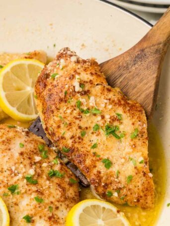 chicken in a white skillet with a spoon shown lifting a piece of chicken