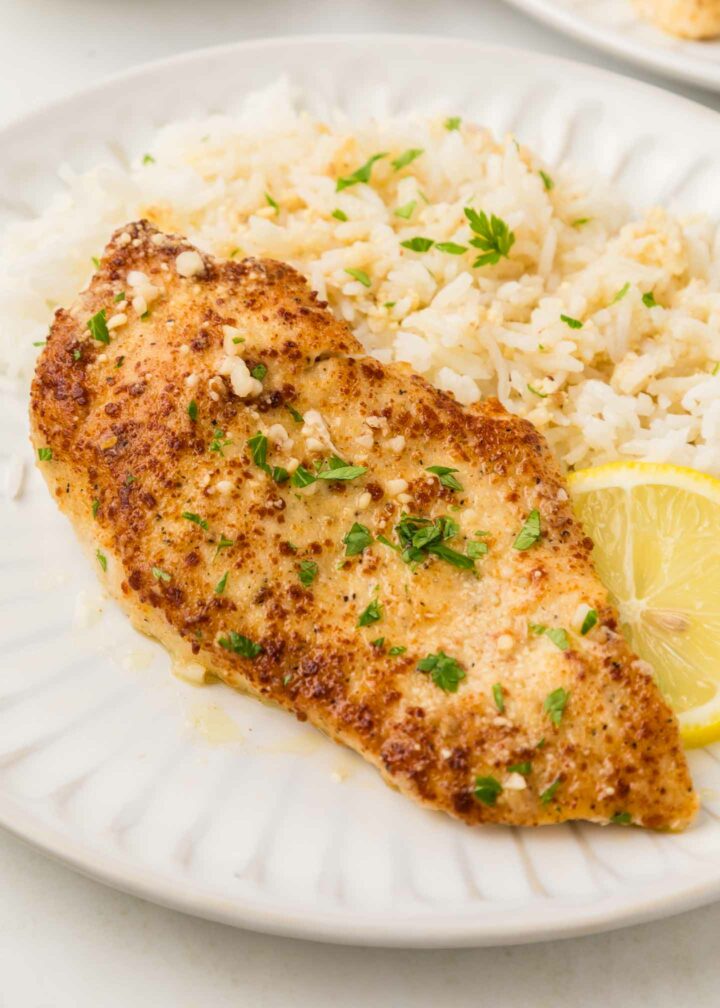 chicken on a white plate with rice and a lemon slice