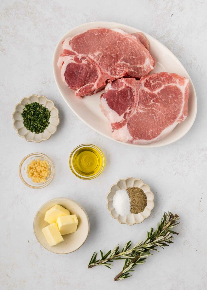 uncooked pork chops on a white plate and rest of ingredients in small bowls