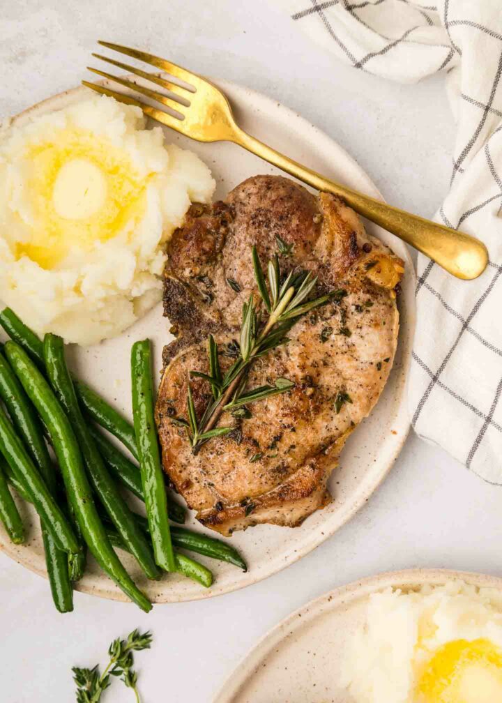 pork chops on a white plate with mashed potatoes and green beans