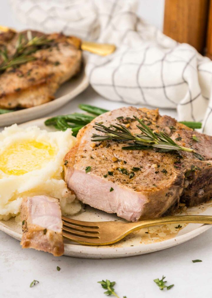 pork chops on a white plate with mashed potatoes and green beans with a bite of pork shown on a fork