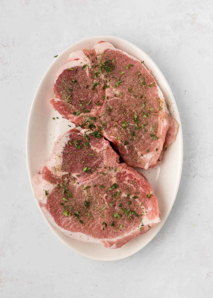 uncooked pork chops seasoned on a white plate