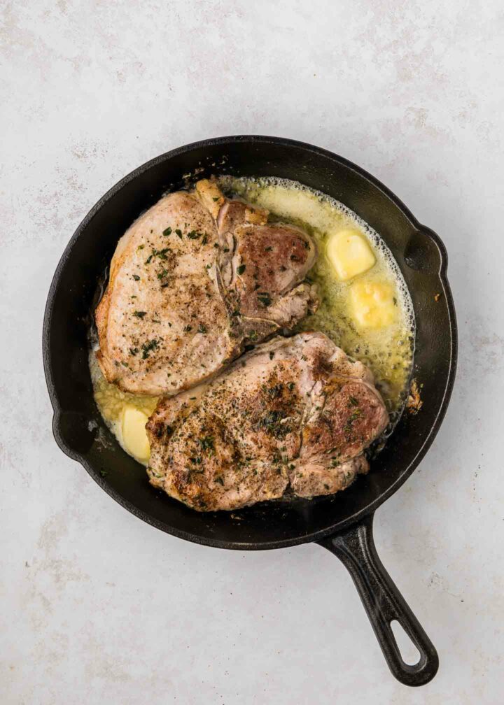 pork chops cooking in a black cast iron skillet with melted butter