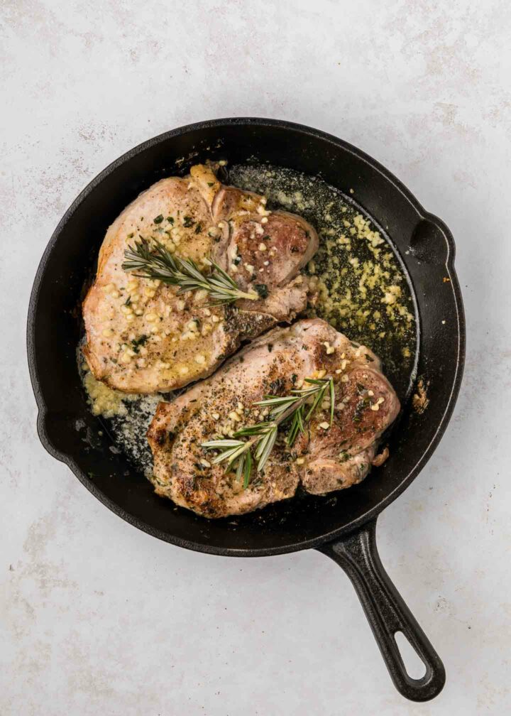 pork chops in black cast iron skillet with herbs and rosemary on top of pork