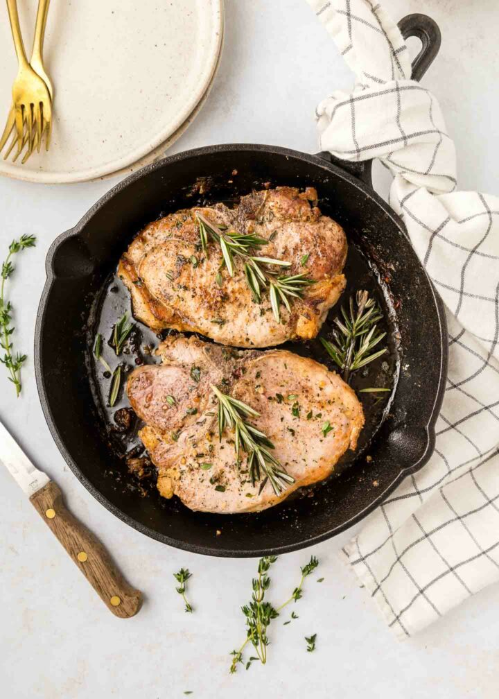 pork chops in a black cast iron skillet with rosemary and herbs