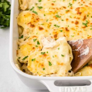 ravioli in a white dish with a wooden spoon lifting up a piece of ravioli and chicken