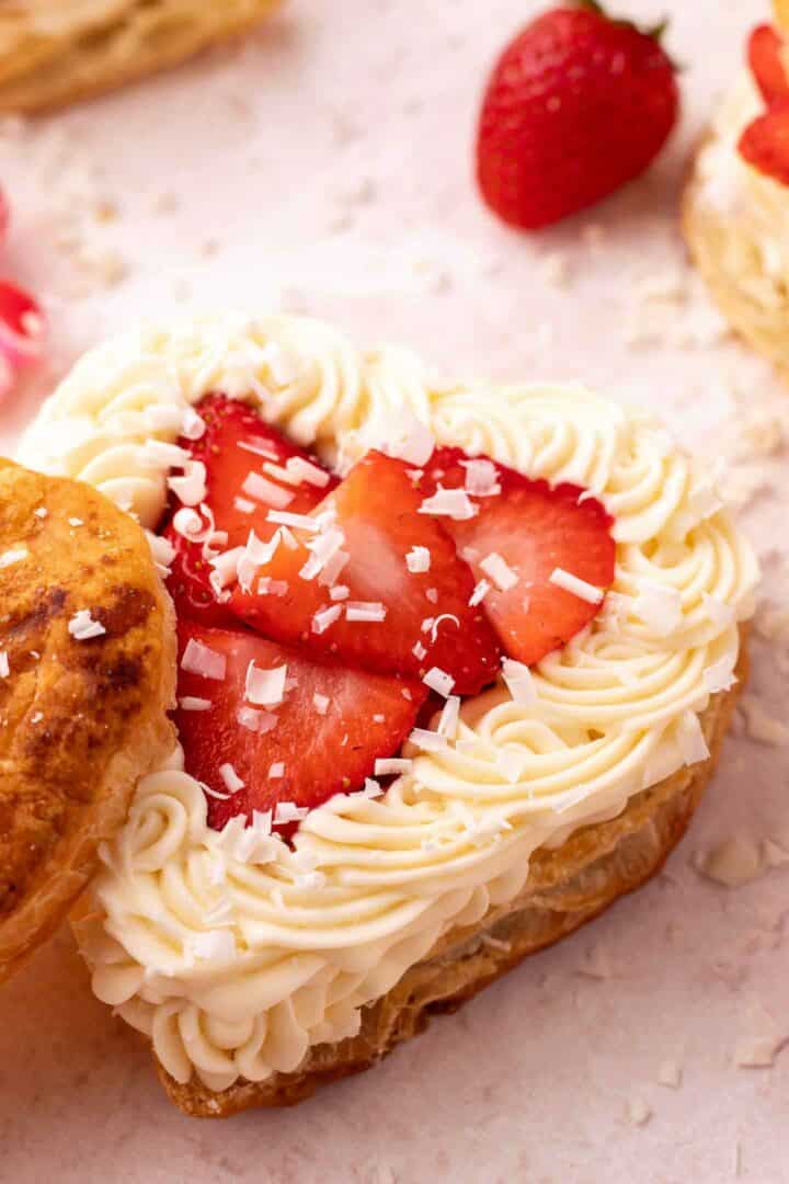 heart puff pastry with white chocolate mousse and sliced strawberries on a light pink surface