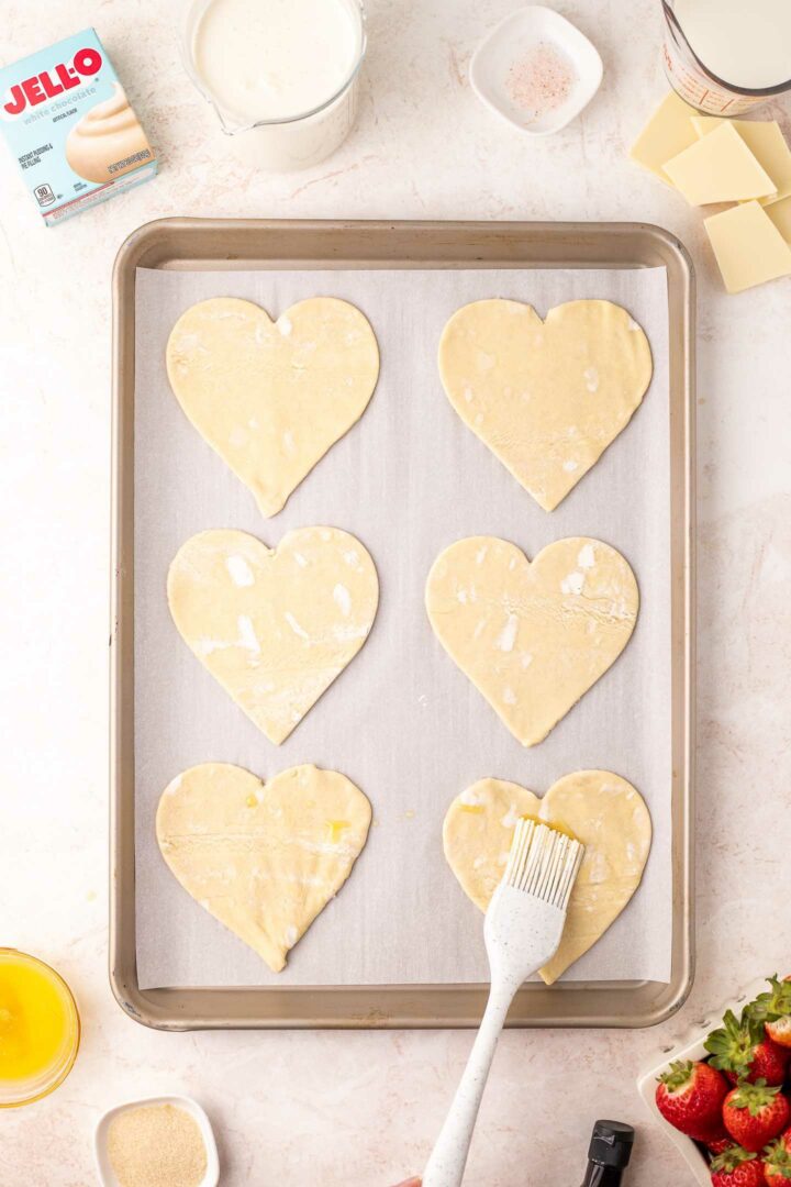 puff pastry hearts on a baking sheet with butter mixture brushed on top