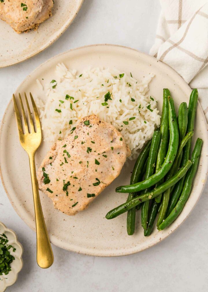 overhead photo of pork chop on a plate with a fork, mashed potatoes, and green beans