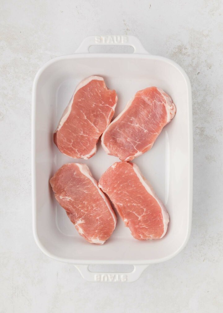 four pork chops in a white baking dish without Greek yogurt mixture