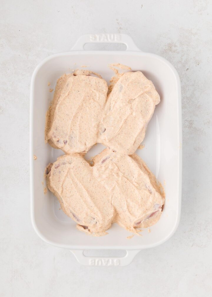 four pork chops in a white baking dish covered with Greek yogurt mixture