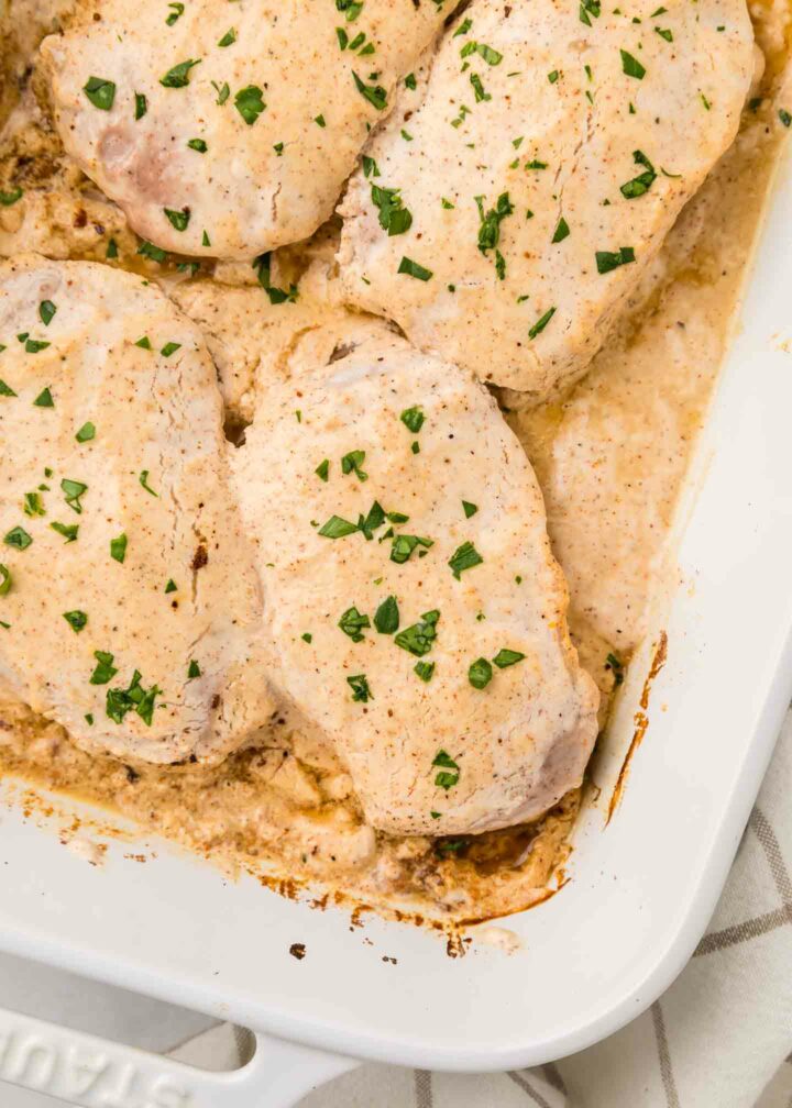 four pork chops shown in a white baking dish