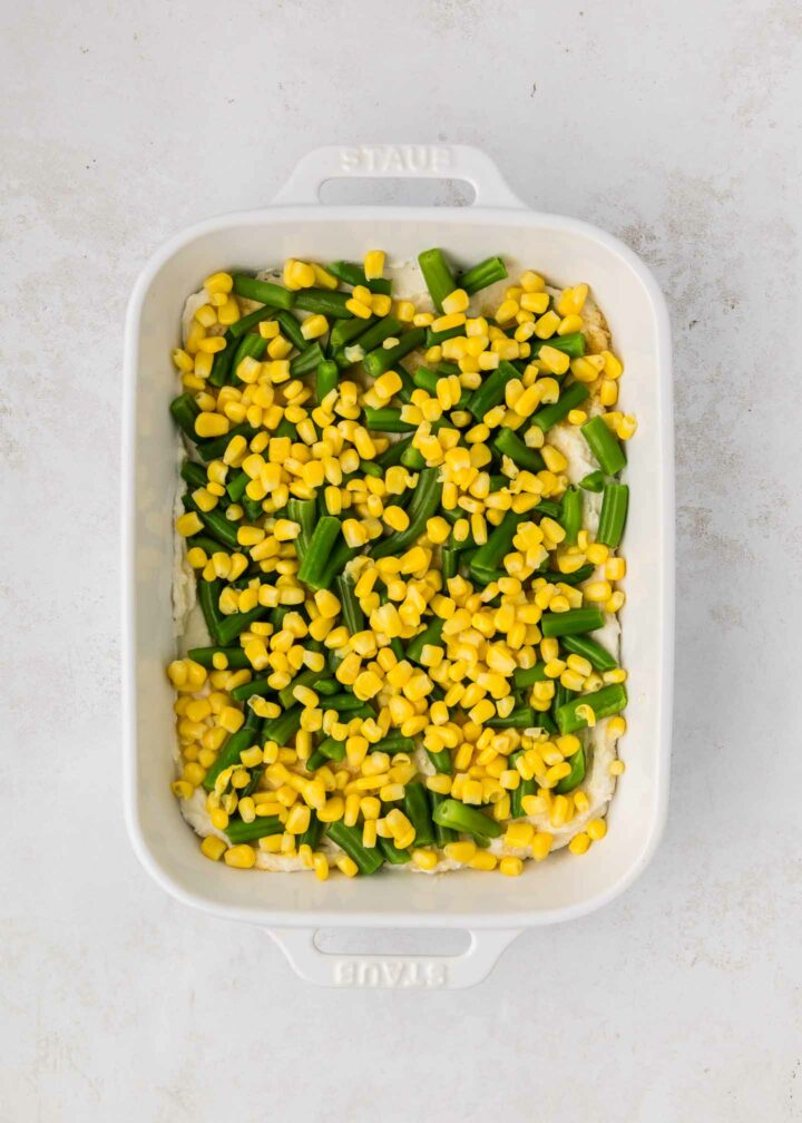 green beans and corn layered on top of mashed potatoes in a white dish