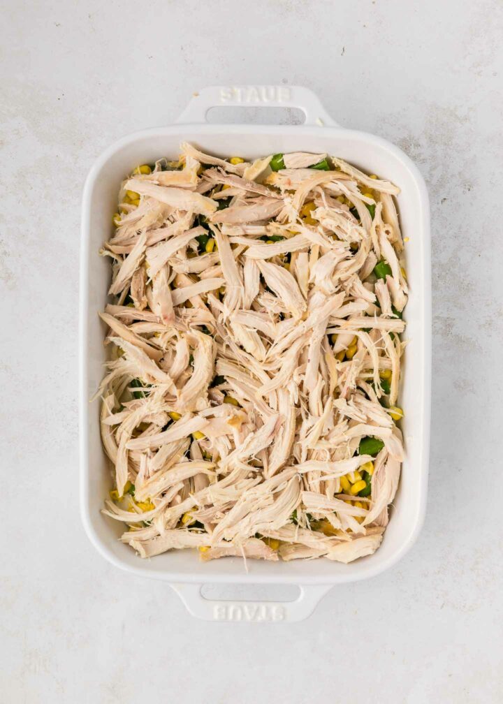 chicken layered on top of green beans and corn in a white dish