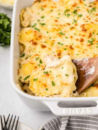 baked ravioli in a white dish with a wooden spoon lifting a piece up